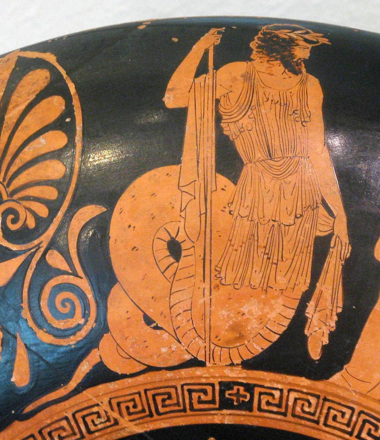 Cecrops holds a royal sceptre, his robed human torso joined to a coiled serpent tail, in a detail of an Attic red-figure cup.