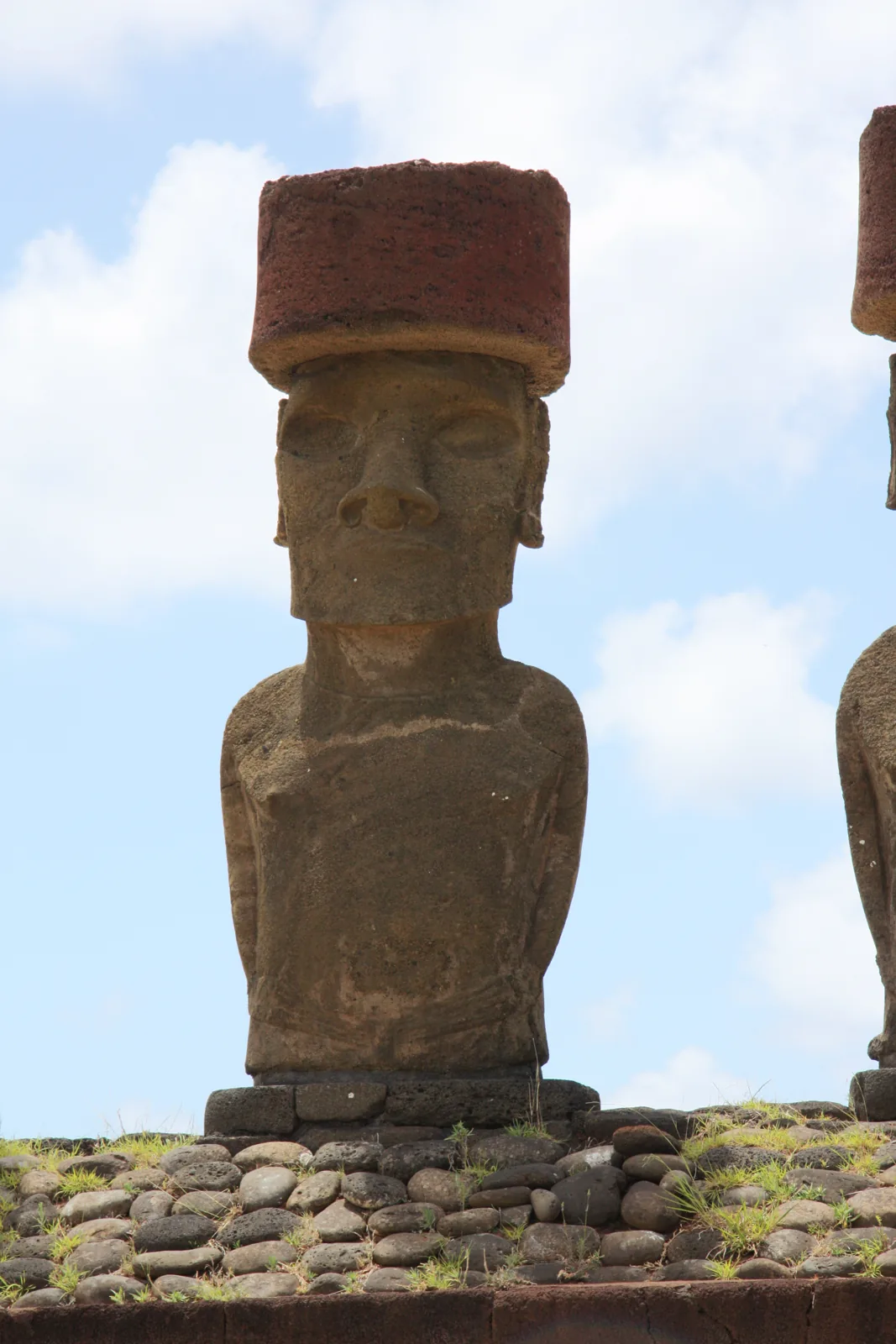 A moai at Ahu Nau Nau with arms alongside its torso, hands turning inward at the lower abdomen, and a red stone pukao above its head.