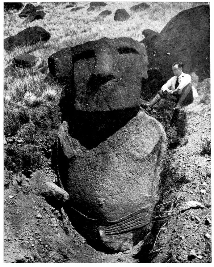 An excavated moai at Rano Raraku showing its complete torso and long carved fingers curving inward across the lower abdomen.